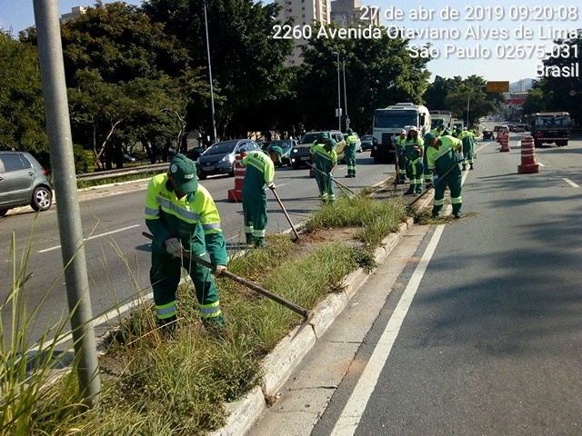 Funcionários devidamente uniformizados (uniforme em tons de verde escuro e claro) realizando o serviço de capina na Avenida Edgar Facó 